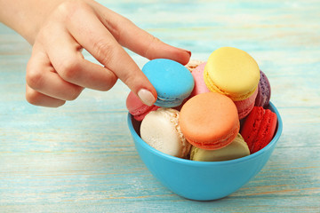 Tasty colorful macaroons in bowl and female hand