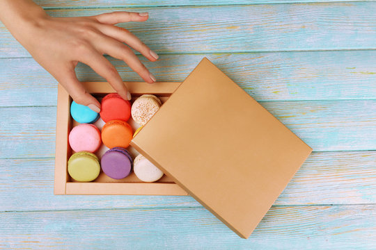 Female hand taking tasty colorful macaroons from box