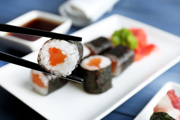 Sushi rolls with salmon on plate, on wooden background