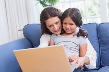 Happy mother and daughter sitting on the couch and using laptop