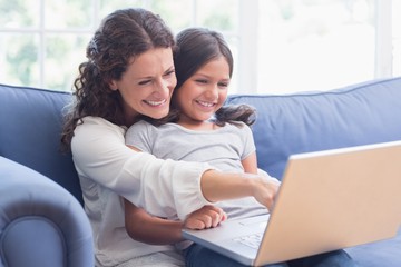 Happy mother and daughter sitting on the couch and using laptop