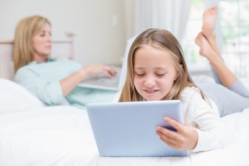 Fototapeta na wymiar Mother using laptop while daughter using tablet pc on the bed