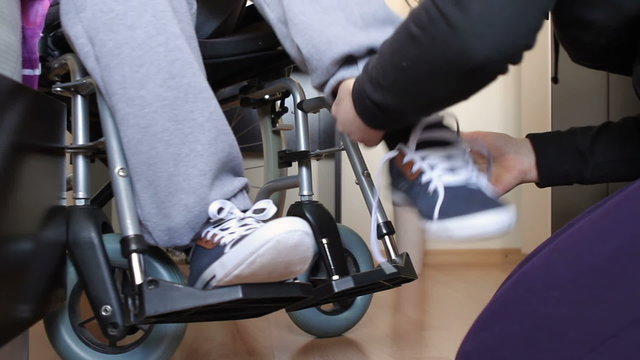 Helping a disabled young man in wheelchair get dressed.