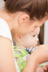 Mother Feeding Her Baby Girl with a Spoon. Mother Giving Food to her adorable Child at Home