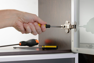A man uses a screwdriver to adjust a concealed hinge fixed on a modern cabinet with a glass door