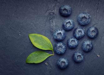 A bunch of delicious blueberries with green leaves on a dark vin