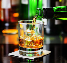 Whiskey pouring from a bottle into a glass in a bar