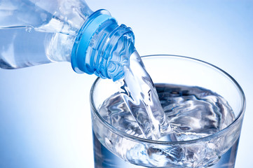 Close-up Pouring glass of water from a plastic bottle on blue ba
