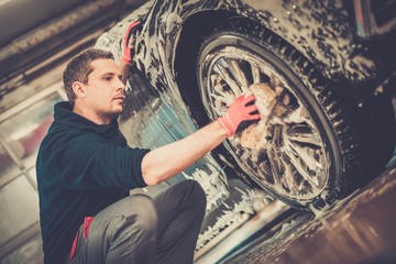Fototapeta na wymiar Man worker washing car's alloy wheels on a car wash