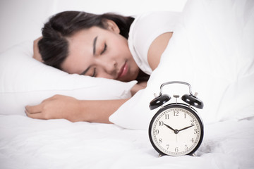 Woman in bed trying to wake up with alarm clock