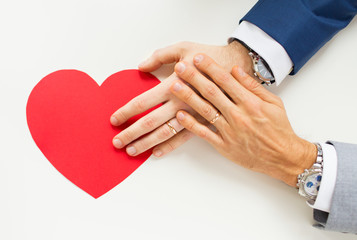 close up of male gay couple hands with red heart