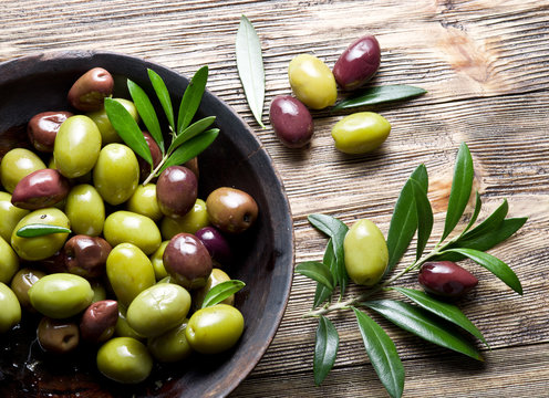 Wooden bowl full of olives and olive twigs besides it.