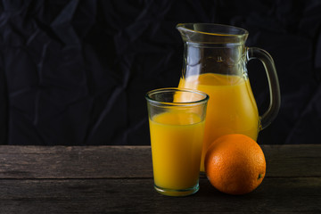 Jug and glass with fresh orange juice, still life art on dark ba