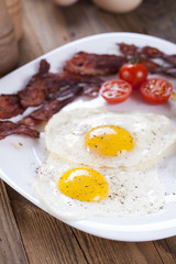 Fried egg and bacon on a plate with spices and vegetables