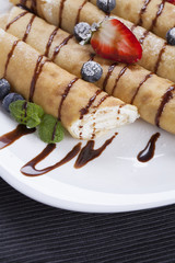 Delicious sweet rolled pancakes on a plate with fresh fruits