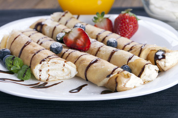 Delicious sweet rolled pancakes on a plate with fresh fruits