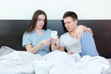 Young woman looking phone with shocked and surprised man next to