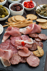 Assorted deli meat snacks, sausages and pickles on a blackboard
