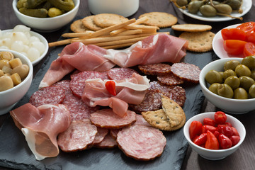 Assorted deli meat snacks, sausages and pickles on a blackboard