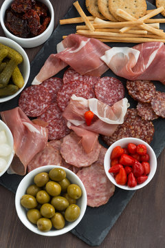 Assorted deli meat snacks, sausages and pickles on a blackboard