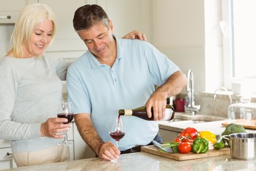 Happy mature couple having red wine while making dinner