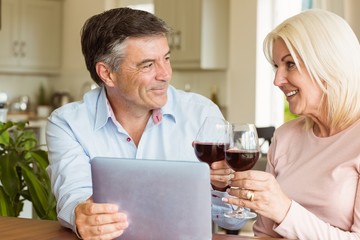 Happy mature couple using tablet drinking red wine