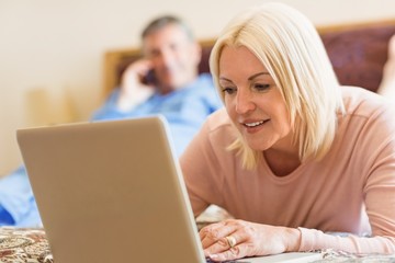Happy mature blonde using laptop on bed