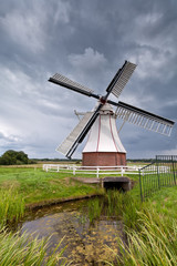 white windmill by river over clouded sky