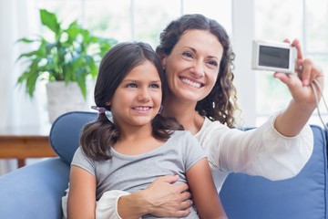Fototapeta premium Happy mother and daughter sitting on the couch and taking selfie