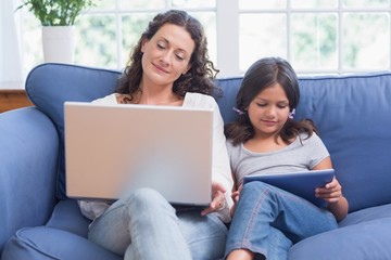 Happy mother and daughter sitting on the couch while using lapto