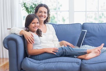 Happy mother and daughter sitting on the couch and using laptop