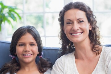 Fototapeta premium Happy mother and daughter sitting on the couch and smiling