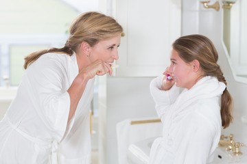 Obraz premium Happy mother and daughter brushing teeth together