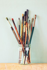 paint brushes in jar over wooden aqua blue background