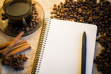 Coffee beans with notebook and a coffee cup on sackcloth.