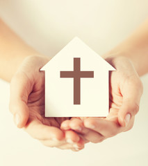 hands holding paper house with cross symbol