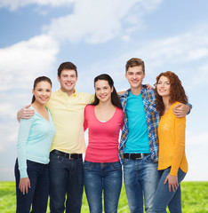 group of smiling teenagers over blue sky and grass