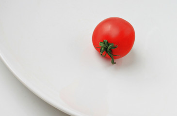 Single fresh cherry tomato on white plate