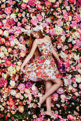A beautiful young girl with flowers bouquet near a floral wall.