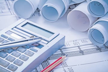 compass on calculator pencil and stack of white rolled up bluepr