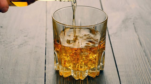 Pouring a scotch whiskey into glass with ice