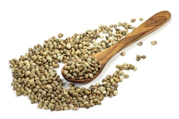 ungeschälte Hanfsamen mit einem Löffel aus Olivenholz isoliert auf weißem Hintergrund