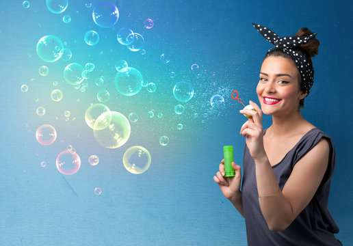 Pretty lady blowing colorful bubbles on blue background