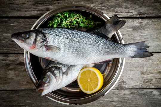 two raw fresh sea bass in a bowl with thyme and lemon