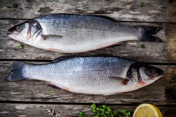 two raw seabass with fresh thyme and lemon on wooden table