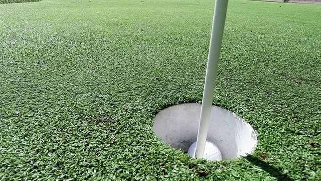 White golf ball rolling in the cup on artificial putting green