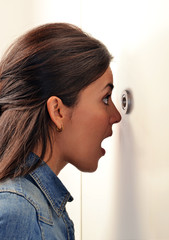 Mujer expresiva viendo a través de ojo mágico,mirilla de puerta.