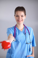 Young woman doctor holding a red heart, standing on gray