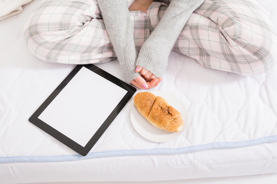 Woman with tablet and croissant in bed