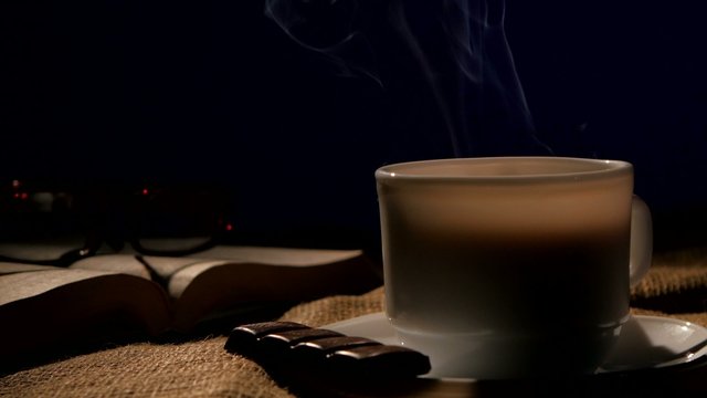 Coffee cup with book, glasses and bar of chocolate, on black
